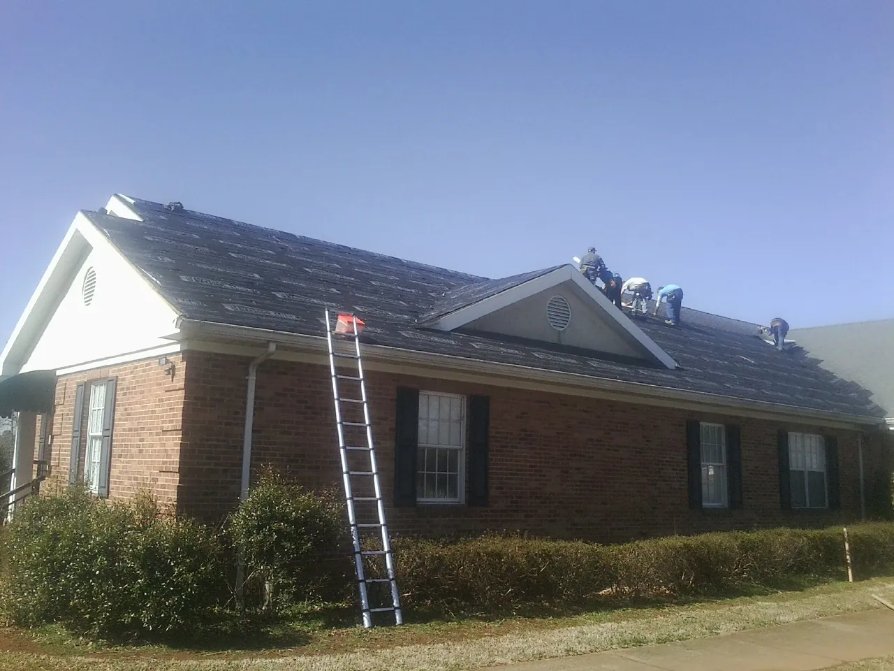 Crew tearing shingles off a brick ranch roof with a ladder set — Metal Roof Repair work by our crew in Montgomery