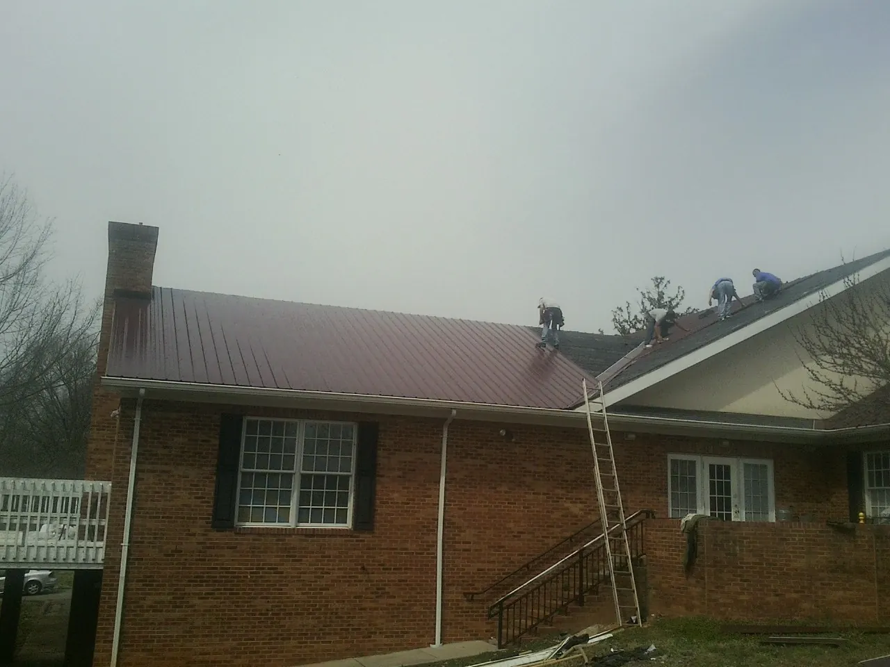 Crew setting red metal roofing panels on a brick home in Montgomery
